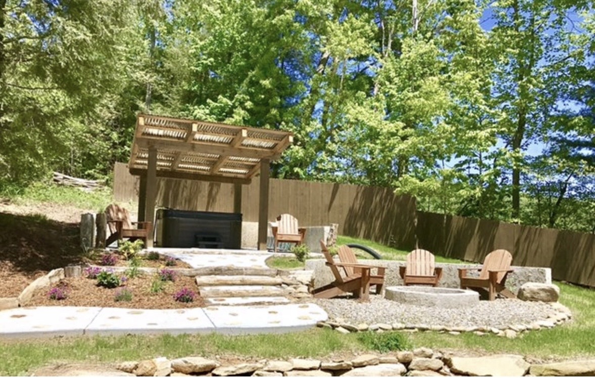 Hot tub under a wood pergola with fire pit and Adirondack chairs