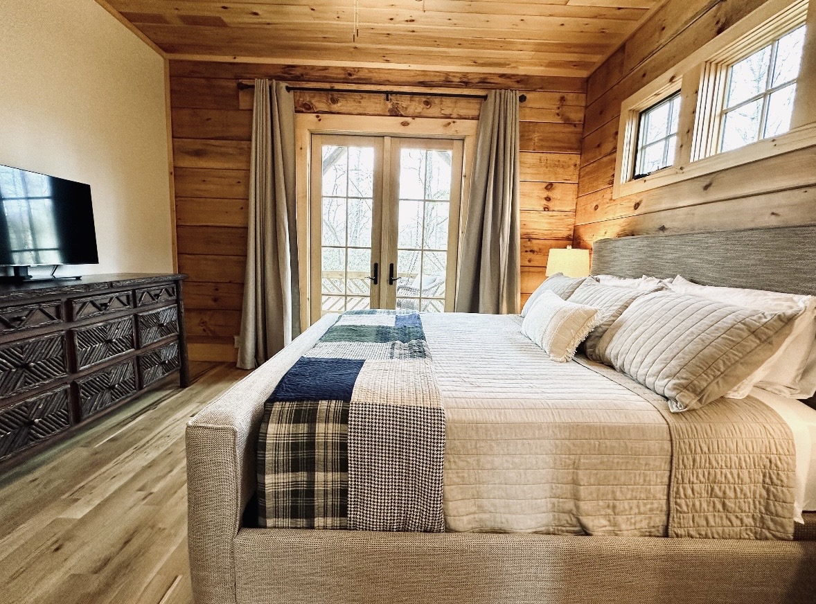 King bedroom with dark wood dresser and French doors to deck